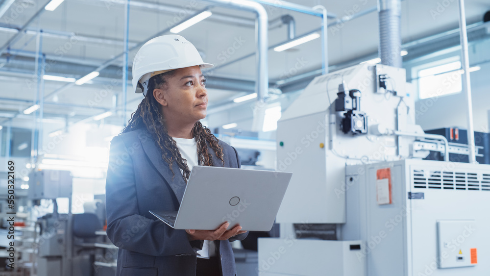 Leinwandbilder portrait of an african female engineer in hard hat standing and using laptop computer at electronic 