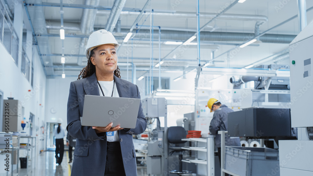 Leinwandbilder Portrait of a Happy Black Female Engineer in Hard Hat Standing and Using Laptop Computer at Electronic Manufacturing Factory. Technician Thinking About Daily Tasks and Working on Development Pipeline.