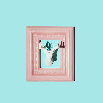 Reindeer head and pink retro style picture frame, creative aesthetic winter holidays inspired layout against pastel blue wall. 