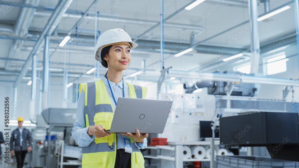 Poster portrait of a happy asian female engineer in hard hat standing and using laptop computer at electron