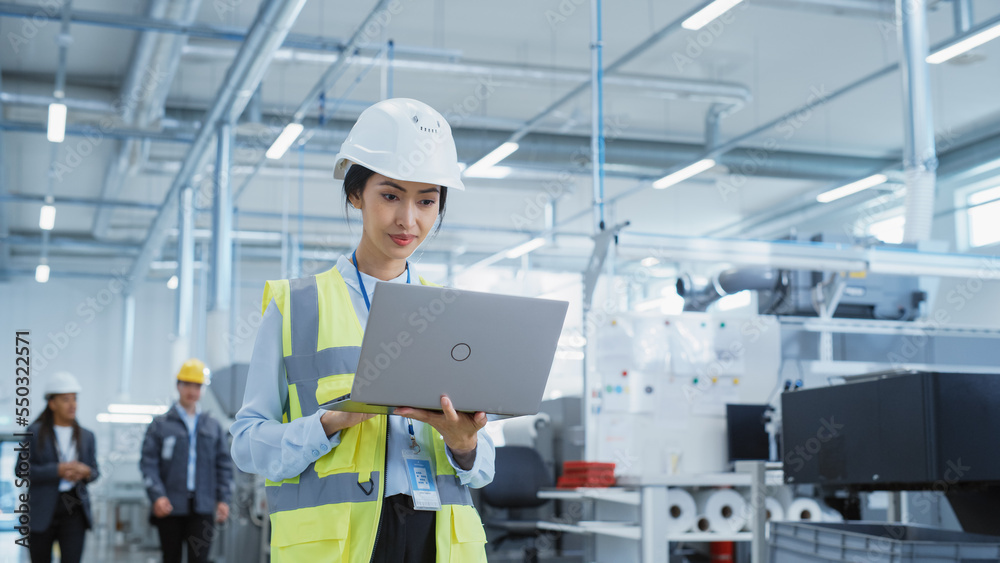 Poster portrait of a happy asian female engineer in hard hat standing and using laptop computer at electron