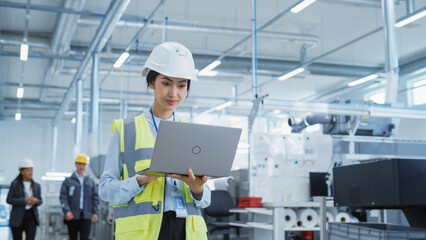 Portrait of a Happy Asian Female Engineer in Hard Hat Standing and Using Laptop Computer at Electronic Manufacturing Factory. Technician Working on Research and Development Production Plan.