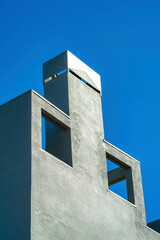 Decorative chimney facade with openings and metal top with gray or blue stucco exterior in the late afternoon sunshine