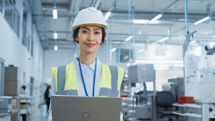 Portrait of a Happy and Smiling Asian Female Engineer in White Hard Hat Standing with Laptop...
