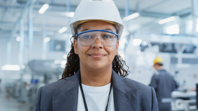 Close Up Portrait of a Successful, Happy and Smiling African Female Engineer in White Hard Hat Standing at Electronics Manufacturing Factory. Black Heavy Industry Specialist Posing for Camera. - Powered by Adobe