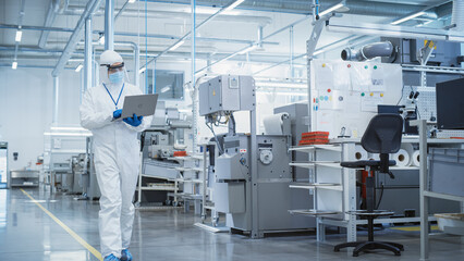 Heavy Industry Manufacturing Factory: Scientist in Sterile Coverall Walking with Laptop Computer,...