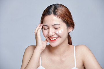 Asia girl applying moisturizing cream on her face. Photo of young asian girl with flawless skin on isolated background. Skin care and beauty concept.