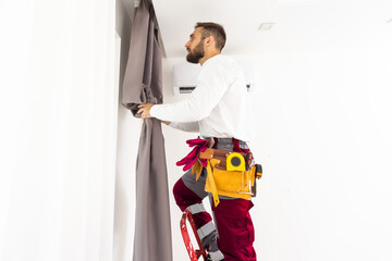 Man hanging window curtain indoors. Interior decor element