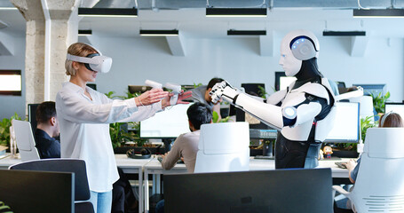 Woman in headset programming robot with metaverse tools. Developer in VR checking work of cyborg by...