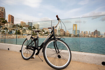 Bicicleta apoyada en el cristal del paseo de Benidorm con sus grandes hoteles de fondo y sobre el mar Mediterráneo azul y tranquilo.
