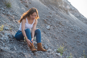 Naklejka premium Asian women backpacking in desert mountains on foot, flipped over and sat on the floor, holding hands on ankles, wearing boots, feeling ankle pain during travel.