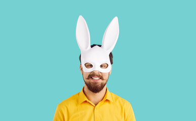 Portrait of cheerful and funny bearded man in rabbit carnival mask isolated on turquoise background. Close up of young man in white rabbit mask with long ears smiling looking at camera. Banner.
