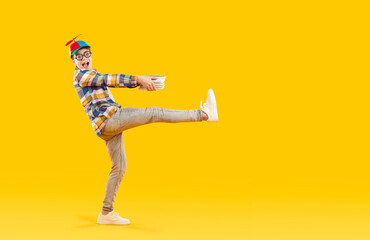 Cheerful preteen boy nerd is funny carrying stack of books on orange background in studio....