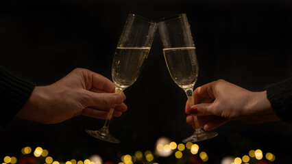 Toast with sparkling wine or champagne glasses on dark black night background with bokwh lights  - Young woman und man holding glass in the hand