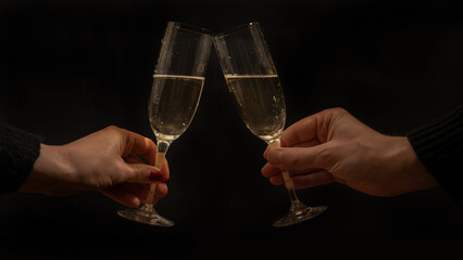 Toast with sparkling wine or champagne glasses on dark black night background - Young woman und man holding glass in the hand