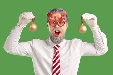 Happy man having fun at Christmas party. Cheerful bearded man in white shirt, striped tie and funny red deer antler glasses holding shiny balls and looking at camera with surprised face expression