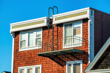 Brown wooden building with white accent color and black balcony with blue and white gradient sky background in neighborhood