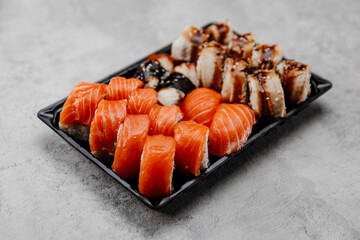 A set of four types of sushi in a black box on a gray background.Side view
