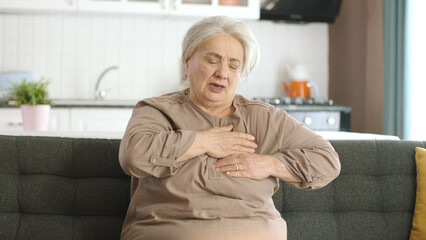 Elderly woman feels pain in her chest. Elderly woman sitting in her armchair at home is having a...