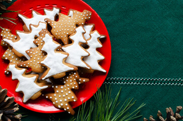 Festive cookies decorated with white icing on a red plate on a green background. Homemade ginger and cinnamon Christmas cookies. Horizontal orientation. Top view. Copy space