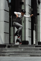 Fototapeta na wymiar Young businessman in roller skates jumping and holding briefcase on urban street.