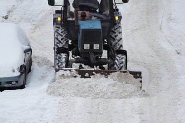 Wheeled bulldozer tractor removes a snow with scraper shovel blade snowplow on road near parked...