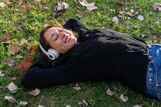 Happy female in headphones lying on grass