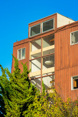 Brown building with wooden exterior or facade with beige or white face with backyard trees and blue and white gradient sky