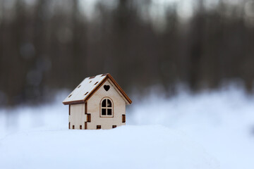 Wooden house model in a snow on winter forest background. Concept of country cottage, real estate in ecologically clean area