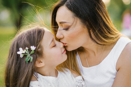 Portrait of a happy mother and daughter in the summer in the park. A mother kisses her daughter. Happy family. Happy Mother's Day. A postcard for Mother's Day.