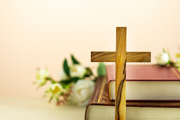 Religion composition with wooden cross with closed red Christian bibles with white flowers on a...