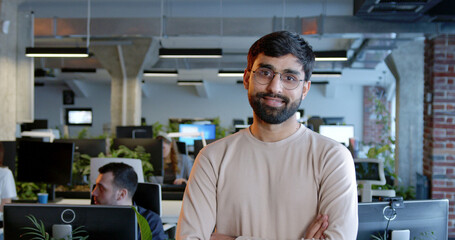 Portrait shot of Arabian successful handsome man looking at camera and smiling in office. Indoor. Cheerful male in glasses standing in comfortable modern coworking space.