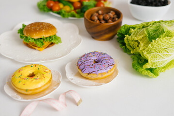 Obraz na płótnie Canvas Healthy or unhealthy food. Conceptual photo of healthy and unhealthy food with measuring tape. Fruits and vegetables vs donuts, sweets and burgers