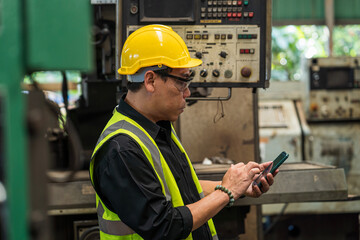 Engineer with mobile phone. Man technician is working in a steel factory. Man worker in safety helmet working on steel machine.