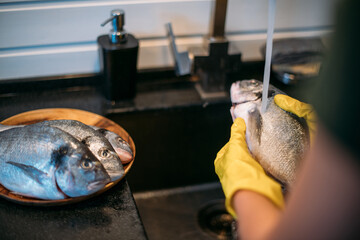 Close-up of hands and fish. A young woman cleans fish at the sink in the kitchen.