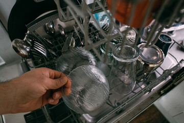 Weekend homework. Close-up of male hands removing clean glass and ceramic dishes from an open dishwasher.