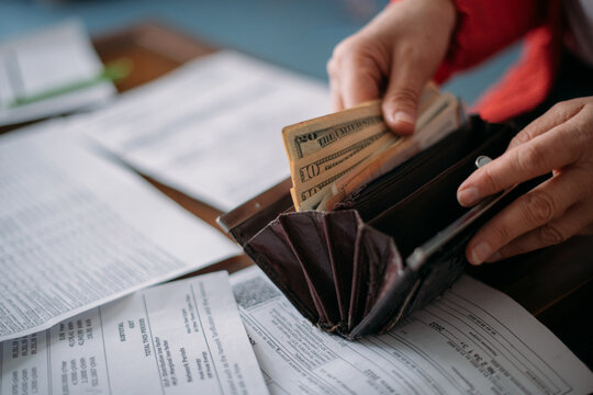 The hands of an elderly woman with a purse with money and a lot of utility bills.