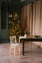 Fototapeta na wymiar Wooden table and white chair in the Christmas living room with a Christmas tree with lights