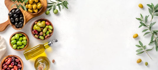 Fototapeten Different olives in bowls on white concrete background. Top view of olives, olive leaves and bottle of olive oil. Diet food concept. Banner. © Tatyana Sidyukova