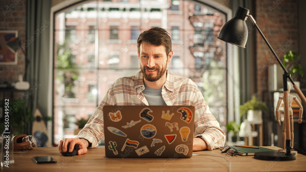 Poster handsome bearded man working on laptop computer while sitting at a table in stylish cozy loft living