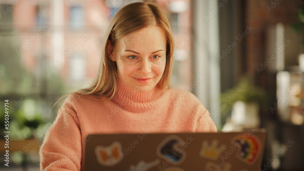 Aufkleber beautiful female working on laptop computer while sitting at a table in stylish cozy loft living roo