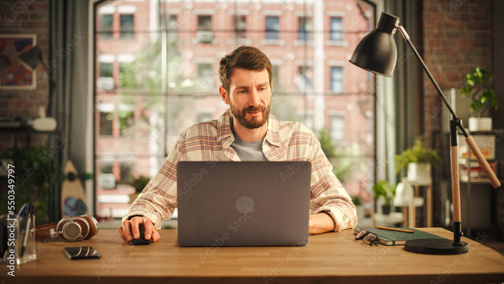 Poster Creative Bearded Man Working on Laptop Computer while Sitting at a Table in Stylish Cozy Loft Living Room. Freelancer Working Remotely. Browsing Internet, Using Social Networks, Thinking on Projects.
