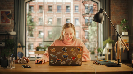 Happy Young Woman Working on Laptop Computer while Sitting in Stylish Creative Office. Successful Freelancer Receiving New Order and Celebrating. Female Winning Lottery and Expressing her Joy.
