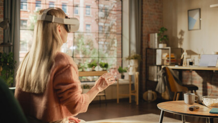 Over the Shoulder Footage of a Female Freelancer Using Virtual Reality Headset and Controllers for Her Project while Sitting on a Couch. Young Woman Working in Futuristic Metaverse App.