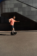 Side view of roller skater in shorts and t-shirt riding on asphalt near building outdoors.