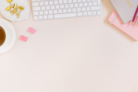 Minimalistic Flat lay women's workspace with a keyboard, pink and beige notepad, colored pencils, paper clips, a cup of tea on a pastel beige background with a copy space
