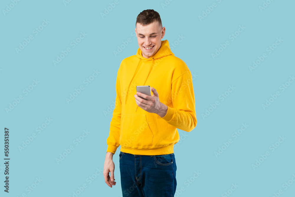 Poster happy young man using cool mobile application on cellphone or texting via smartphone, blue studio ba