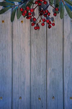 Wintertime rustic background with decorative rowan berry twigs with green leaves and red berry. Flat lay, top view, space for text, copy-space on toned wooden planks.