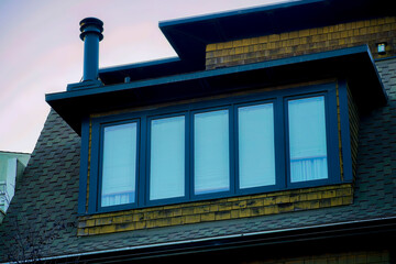 Fototapeta premium Decorative bay style window with vertical glass pannels on dark roof with urban tiles in the suburban part of the neighborhood