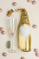 Champagne bottle decorated hat of dwarf with golden sequins, crystal wine glasses, Christmas and New Year party concept, still life pattern with alcohol drinks. Minimal monochrome beige gold